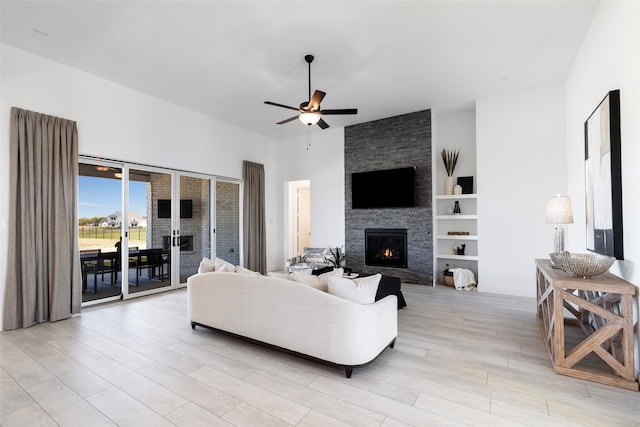 living room featuring ceiling fan, a stone fireplace, light wood-type flooring, and built in shelves