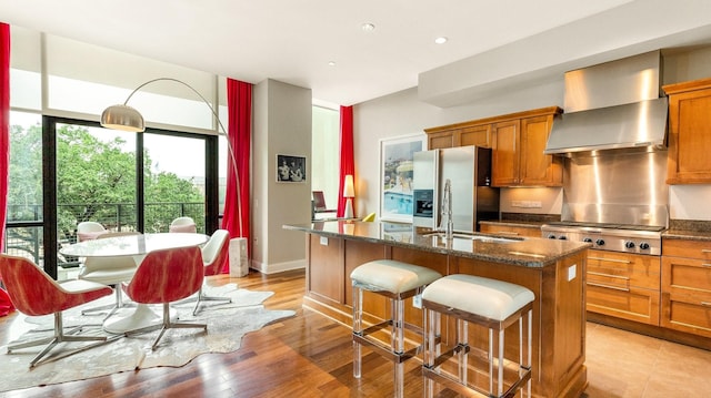 kitchen with sink, wall chimney exhaust hood, stainless steel appliances, dark stone countertops, and light hardwood / wood-style floors