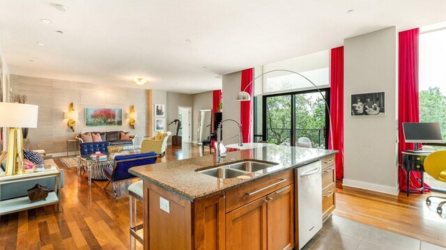 kitchen with sink, dark stone countertops, an island with sink, appliances with stainless steel finishes, and hardwood / wood-style flooring