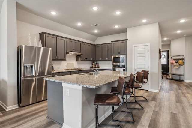 kitchen featuring light stone countertops, a center island with sink, hardwood / wood-style floors, and appliances with stainless steel finishes