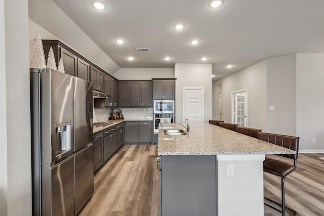 kitchen featuring light stone countertops, sink, a center island with sink, appliances with stainless steel finishes, and hardwood / wood-style flooring