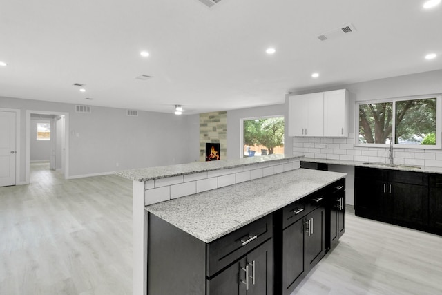 kitchen with light wood-type flooring, sink, white cabinets, a kitchen island, and a tiled fireplace