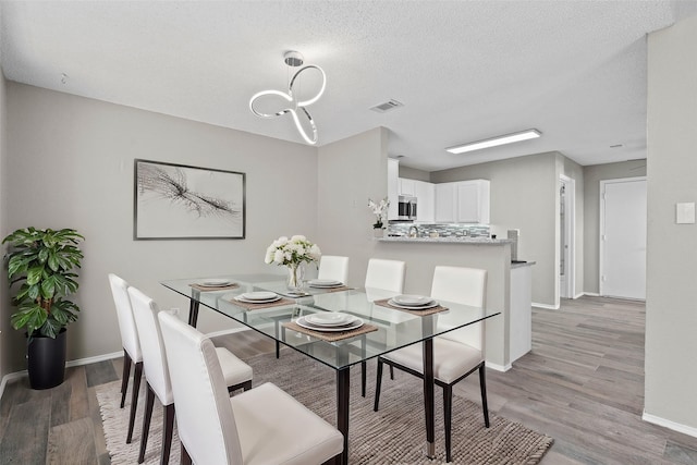 dining space with light hardwood / wood-style floors, a textured ceiling, and a chandelier