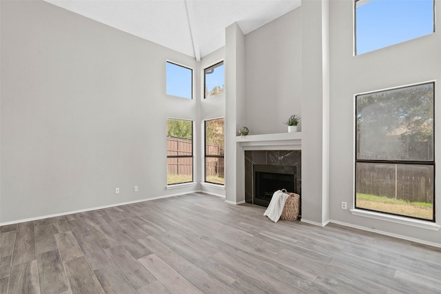 unfurnished living room with a high end fireplace, light hardwood / wood-style floors, and high vaulted ceiling