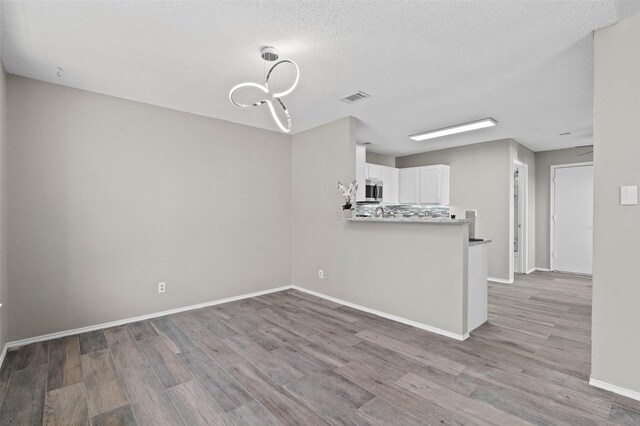 kitchen featuring pendant lighting, white cabinets, light hardwood / wood-style flooring, a textured ceiling, and kitchen peninsula