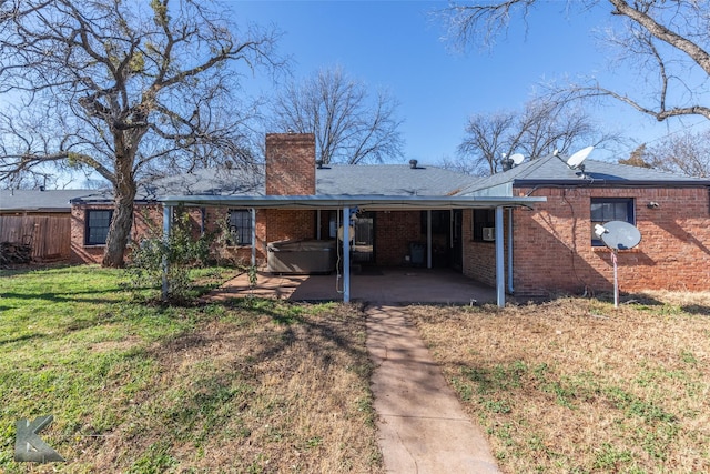 back of property with a yard, a hot tub, and a patio