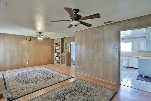 living room with light hardwood / wood-style flooring, wooden walls, and ceiling fan