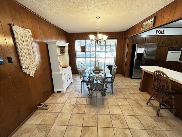 tiled dining area with an inviting chandelier, a textured ceiling, and wood walls