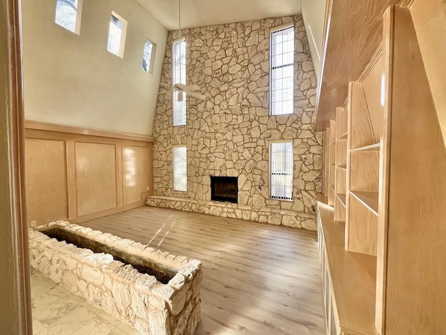 unfurnished living room with a towering ceiling, a healthy amount of sunlight, a fireplace, and light hardwood / wood-style flooring