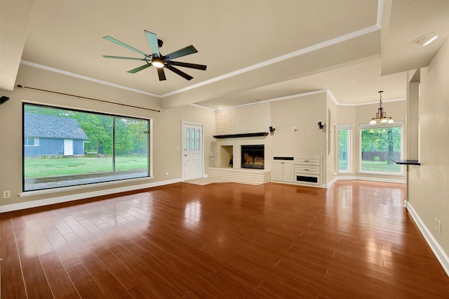 unfurnished living room with ceiling fan with notable chandelier, plenty of natural light, hardwood / wood-style floors, and a brick fireplace