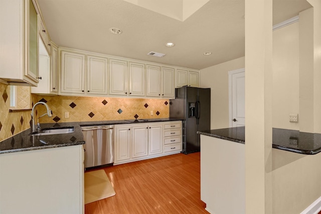 kitchen featuring sink, black fridge, light hardwood / wood-style flooring, stainless steel dishwasher, and backsplash