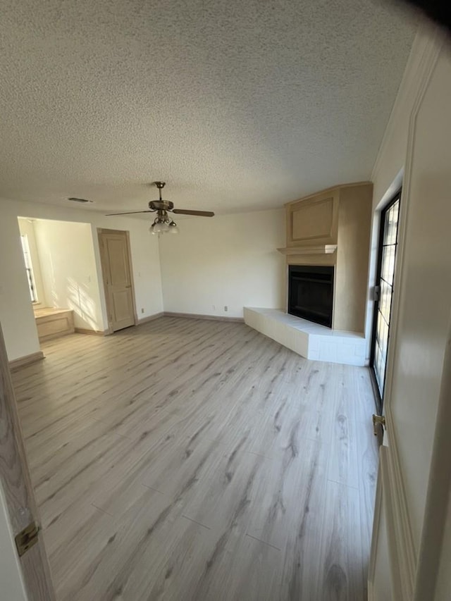 unfurnished living room featuring ceiling fan, a textured ceiling, and light wood-type flooring