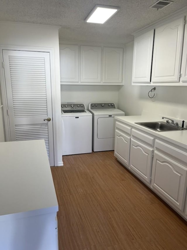 clothes washing area with dark wood-type flooring, washing machine and clothes dryer, sink, cabinets, and a textured ceiling