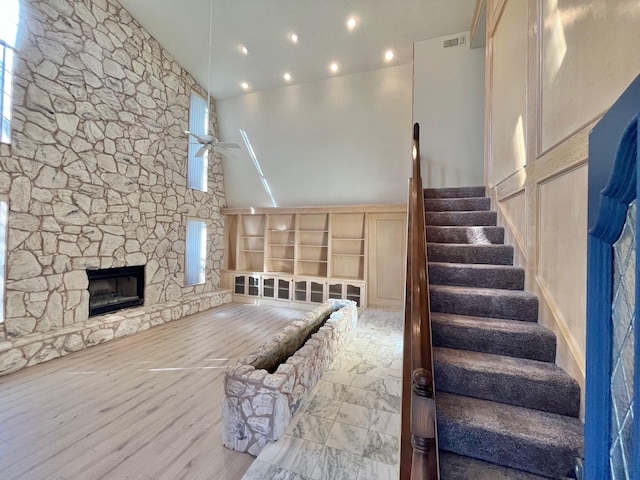 unfurnished living room with ceiling fan, a fireplace, hardwood / wood-style floors, and a high ceiling