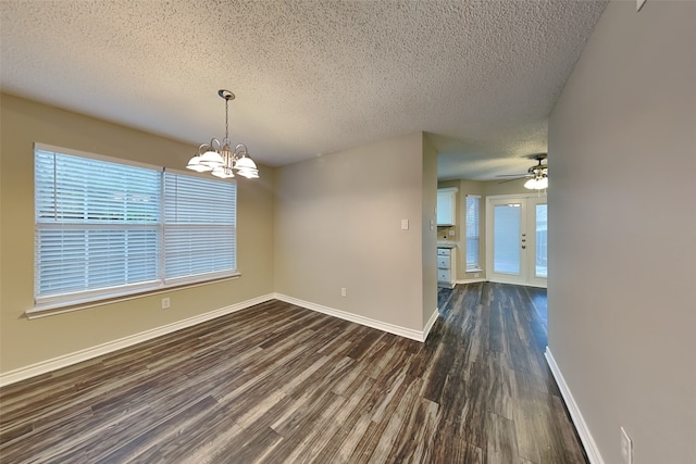 unfurnished dining area featuring a textured ceiling, ceiling fan with notable chandelier, dark wood-type flooring, and french doors