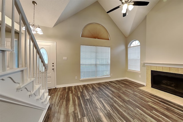 unfurnished living room with ceiling fan with notable chandelier, a tile fireplace, dark wood-type flooring, and high vaulted ceiling