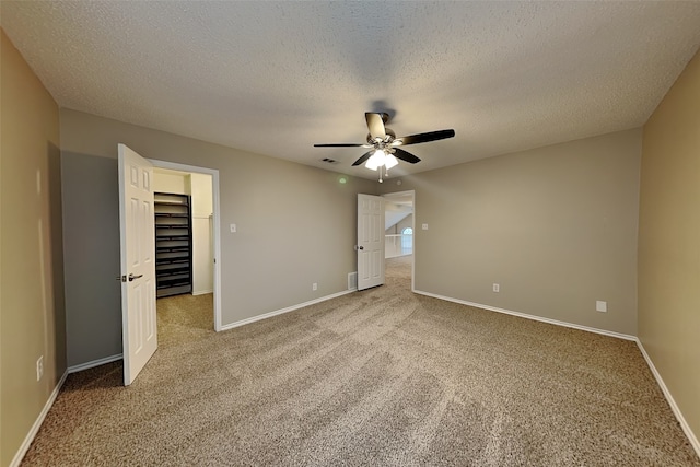 unfurnished bedroom featuring ceiling fan, a spacious closet, light carpet, and a textured ceiling