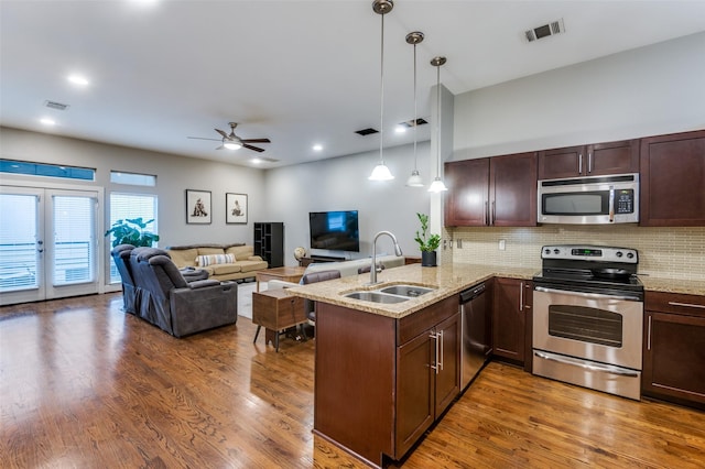 kitchen with kitchen peninsula, stainless steel appliances, sink, decorative light fixtures, and dark hardwood / wood-style floors