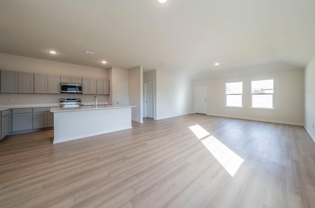 kitchen with sink, gray cabinetry, a kitchen island with sink, stainless steel appliances, and light hardwood / wood-style flooring