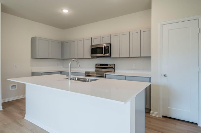 kitchen with a kitchen island with sink, sink, light hardwood / wood-style flooring, and appliances with stainless steel finishes