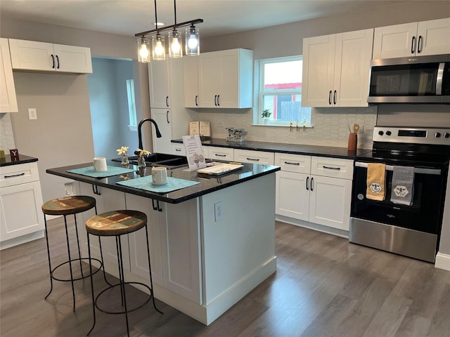 kitchen with dark wood-type flooring, a center island with sink, white cabinets, sink, and stainless steel appliances