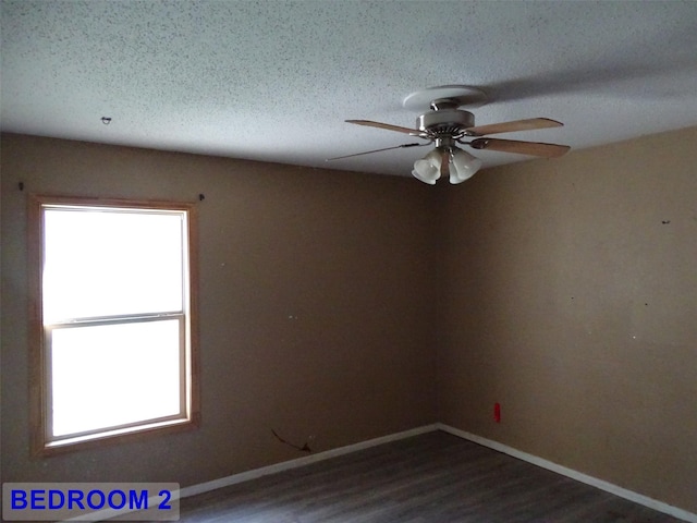 spare room featuring a textured ceiling, dark wood-type flooring, ceiling fan, and a healthy amount of sunlight