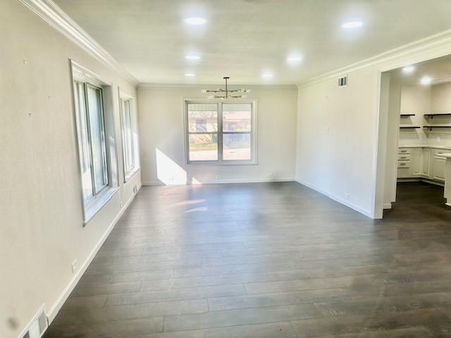 empty room with dark hardwood / wood-style flooring, ornamental molding, and a chandelier