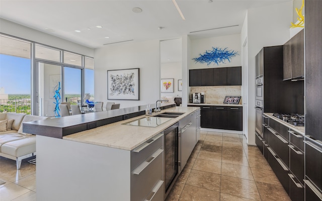 kitchen featuring sink, wine cooler, backsplash, an island with sink, and appliances with stainless steel finishes