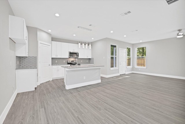 kitchen with a kitchen island with sink, appliances with stainless steel finishes, decorative light fixtures, light hardwood / wood-style floors, and white cabinetry