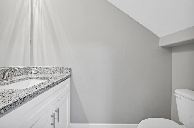 bathroom featuring toilet, vanity, and vaulted ceiling