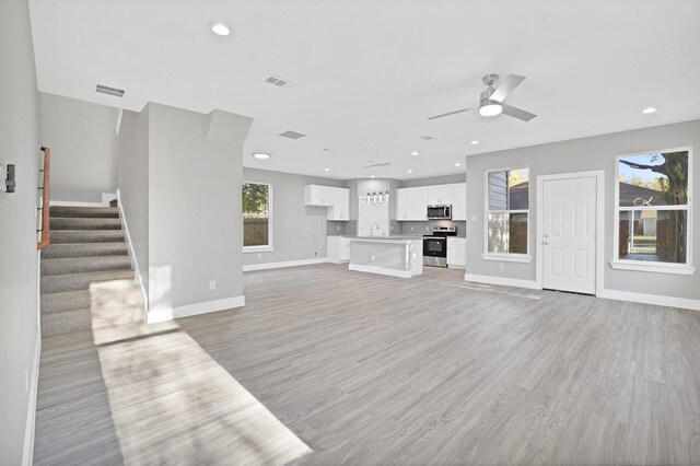 unfurnished living room featuring ceiling fan, sink, and light wood-type flooring