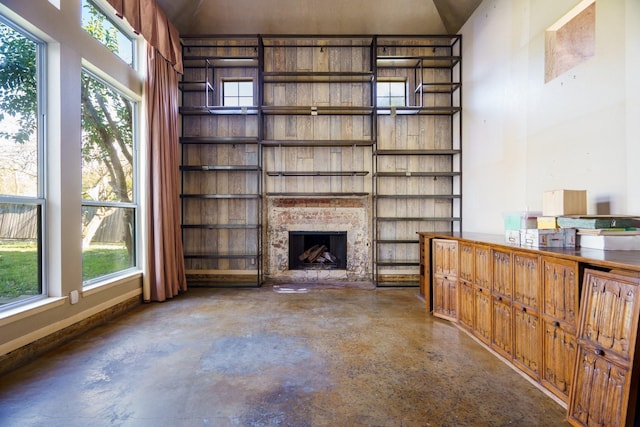 unfurnished living room with concrete flooring, vaulted ceiling, a brick fireplace, and a healthy amount of sunlight