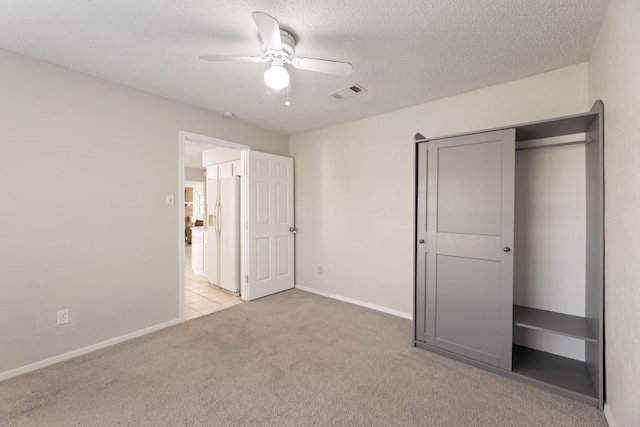 unfurnished bedroom with a textured ceiling, light colored carpet, white fridge with ice dispenser, and ceiling fan