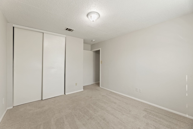 unfurnished bedroom featuring a textured ceiling, light colored carpet, and a closet