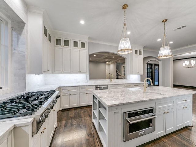 kitchen with pendant lighting, dark wood-type flooring, an island with sink, appliances with stainless steel finishes, and white cabinetry