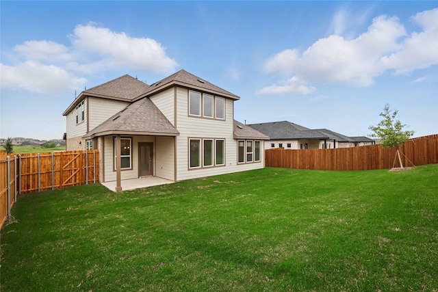 back of property with a fenced backyard, a yard, a patio area, and roof with shingles