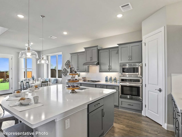 kitchen with stainless steel appliances, hanging light fixtures, gray cabinetry, and dark hardwood / wood-style floors