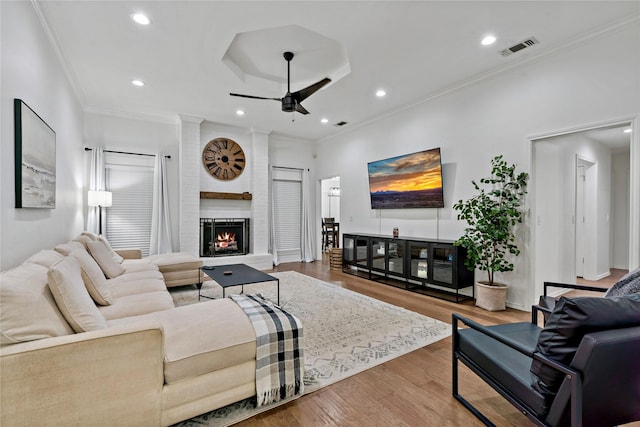 living room featuring hardwood / wood-style floors, a brick fireplace, ceiling fan, and crown molding