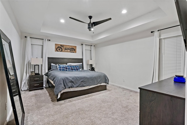 carpeted bedroom with a raised ceiling and ceiling fan