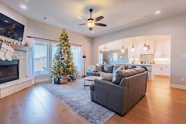 living room featuring ceiling fan with notable chandelier, light hardwood / wood-style floors, sink, and a fireplace