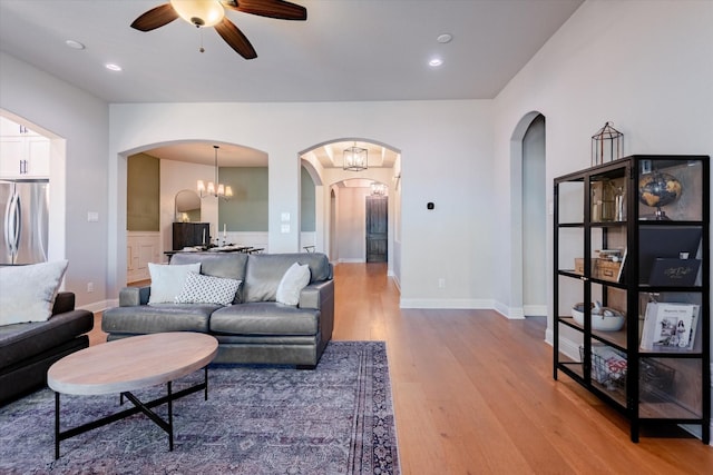 living room featuring ceiling fan with notable chandelier and light wood-type flooring