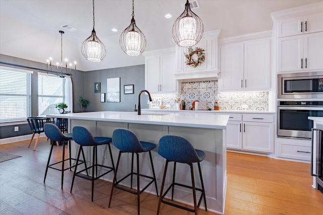 kitchen with white cabinetry, stainless steel appliances, hanging light fixtures, and an island with sink