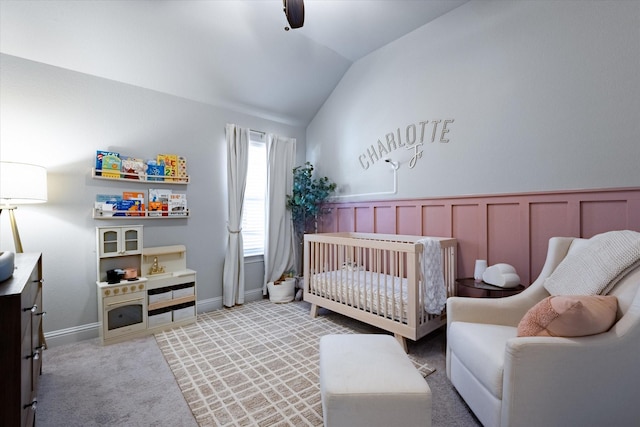 carpeted bedroom featuring a crib, vaulted ceiling, and ceiling fan