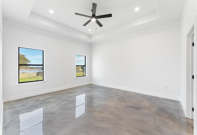 empty room featuring ceiling fan, a raised ceiling, and concrete floors