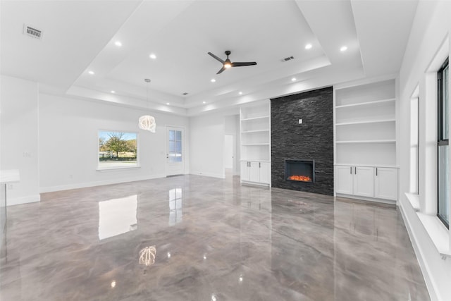 unfurnished living room featuring a tray ceiling, built in shelves, ceiling fan, and a fireplace