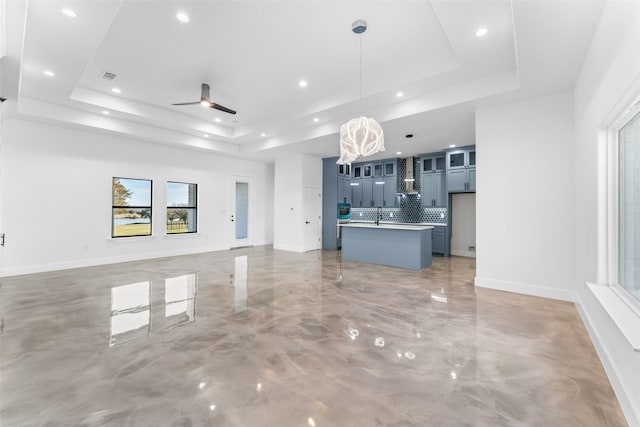 unfurnished living room with a tray ceiling, ceiling fan, and sink