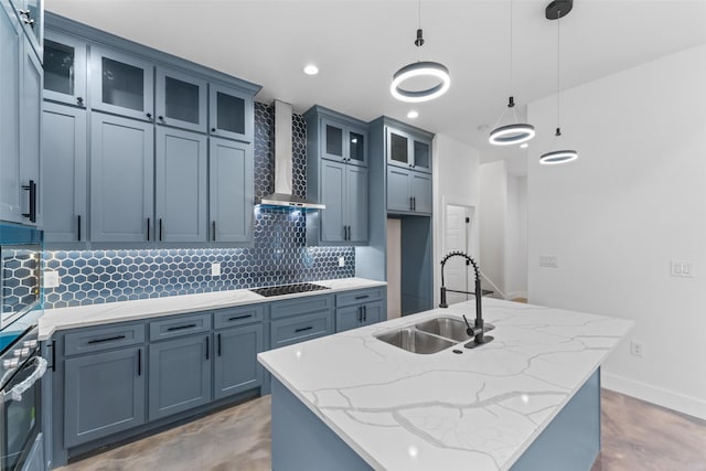 kitchen with sink, wall chimney range hood, an island with sink, pendant lighting, and oven