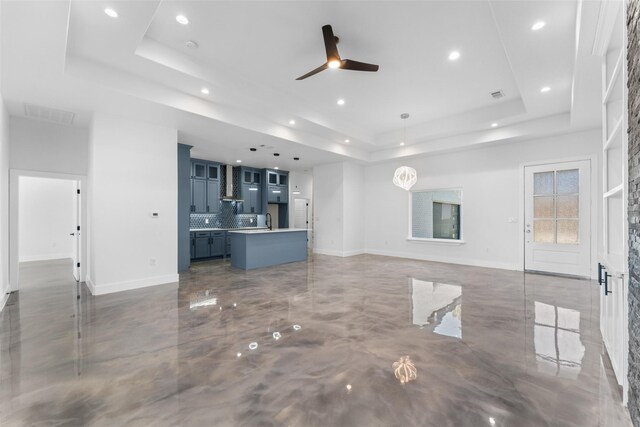 unfurnished living room featuring a tray ceiling and ceiling fan