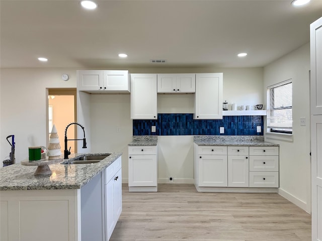 kitchen featuring white cabinetry, sink, light stone countertops, and light wood-type flooring