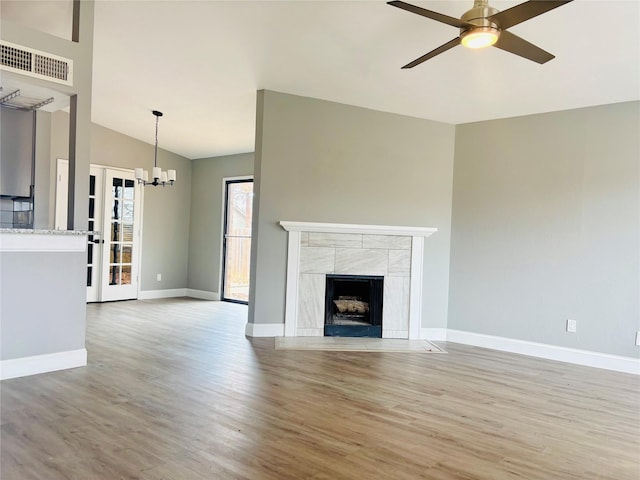 unfurnished living room featuring ceiling fan with notable chandelier, lofted ceiling, a fireplace, and light hardwood / wood-style flooring